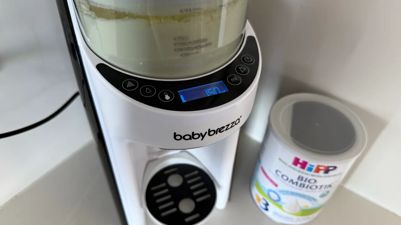 A Baby Brezza formula machine on a counter, its container part filled with powder and its screen lit, and beside it a tin of HiPP Bio Combiotik Stage 3.