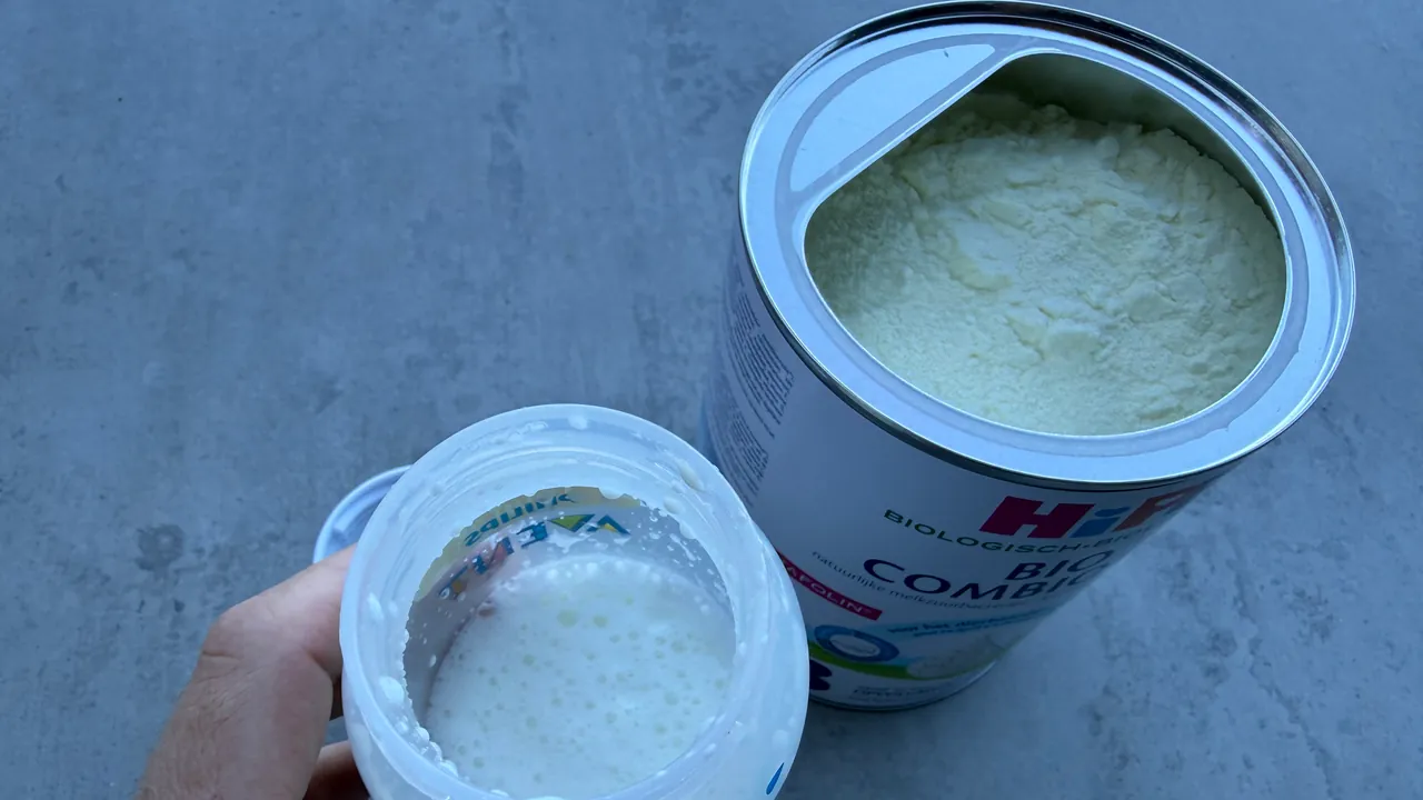 A hand holding an open bottle of freshly shaken formula with foam on top, beside an open tin of HiPP Bio Combiotik with small lumps in its powder.