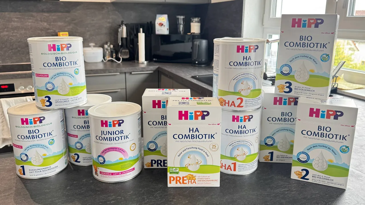 Eleven HiPP formula packs stacked on a kitchen counter: Dutch Bio Combiotik tins and the Junior on the left, German Bio Combiotik PRE and HA Combiotik PRE boxes in the middle, Dutch HA Combiotik 2 on 1 tins, and German Bio Combiotik 1, 2 and 3 boxes on the right.