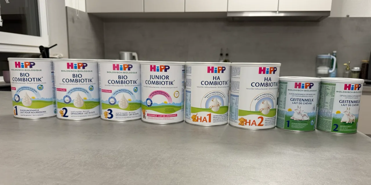 Eight HiPP Dutch formula tins in a row on a kitchen counter, fronts to the camera: Bio Combiotik 1, 2 and 3, Junior Combiotik, HA Combiotik 1 and 2, and goat's milk 1 and 2.