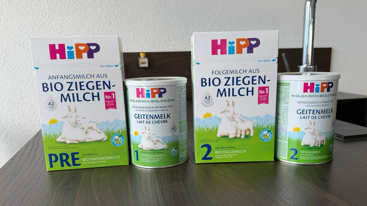 Four HiPP goat's milk formula packs on a kitchen counter, fronts to the camera: the German PRE box, the Dutch Stage 1 tin, the German Stage 2 box and the Dutch Stage 2 tin.