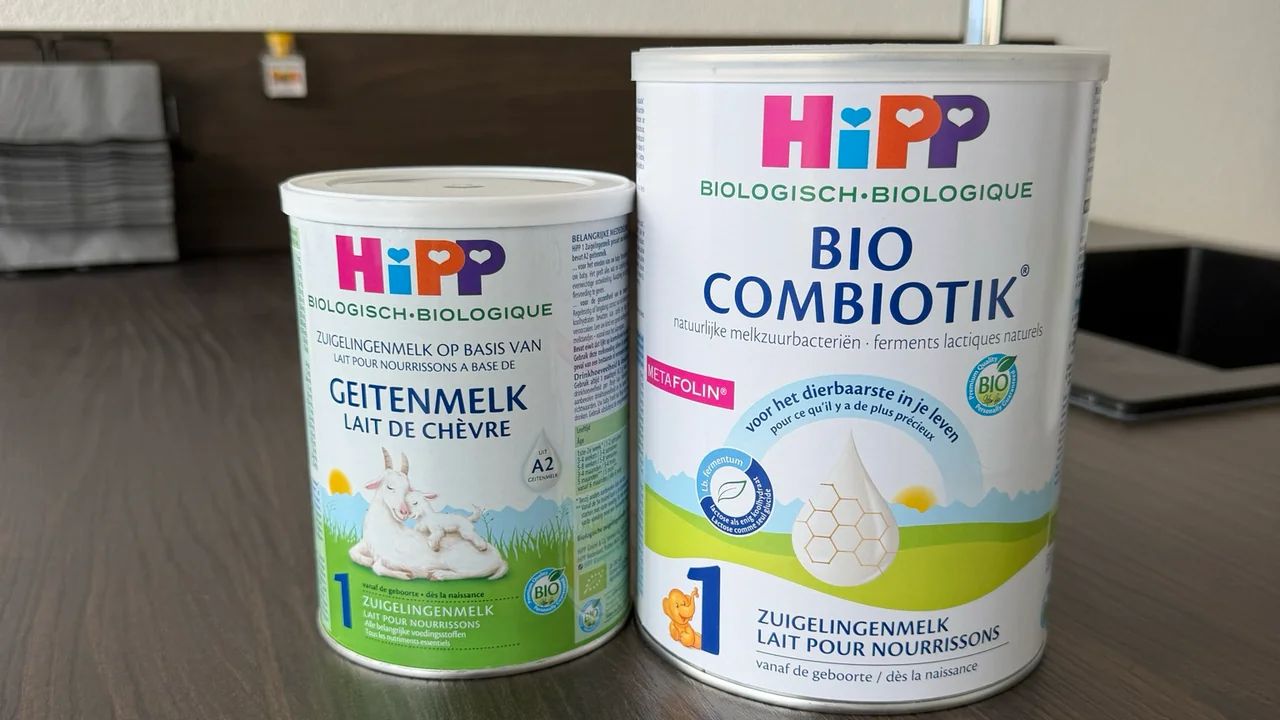 Two Dutch HiPP Stage 1 tins side by side on a kitchen counter, fronts to the camera: the smaller goat's milk tin on the left and the larger Bio Combiotik tin on the right.