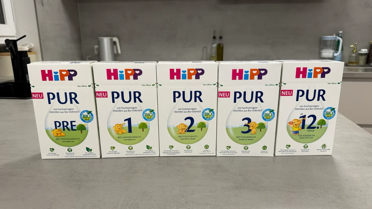 Five HiPP PUR boxes in a row on a kitchen counter, fronts to the camera: PRE, 1, 2, 3 and the Kindermilch.
