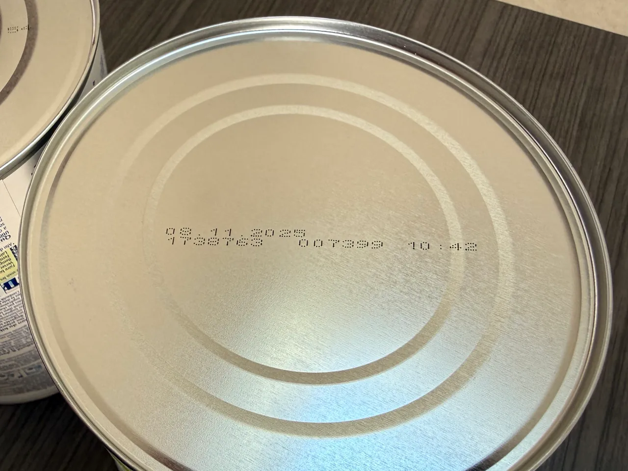 The base of a HiPP tin, close, with a date on the first printed line and two codes and a time on the second.